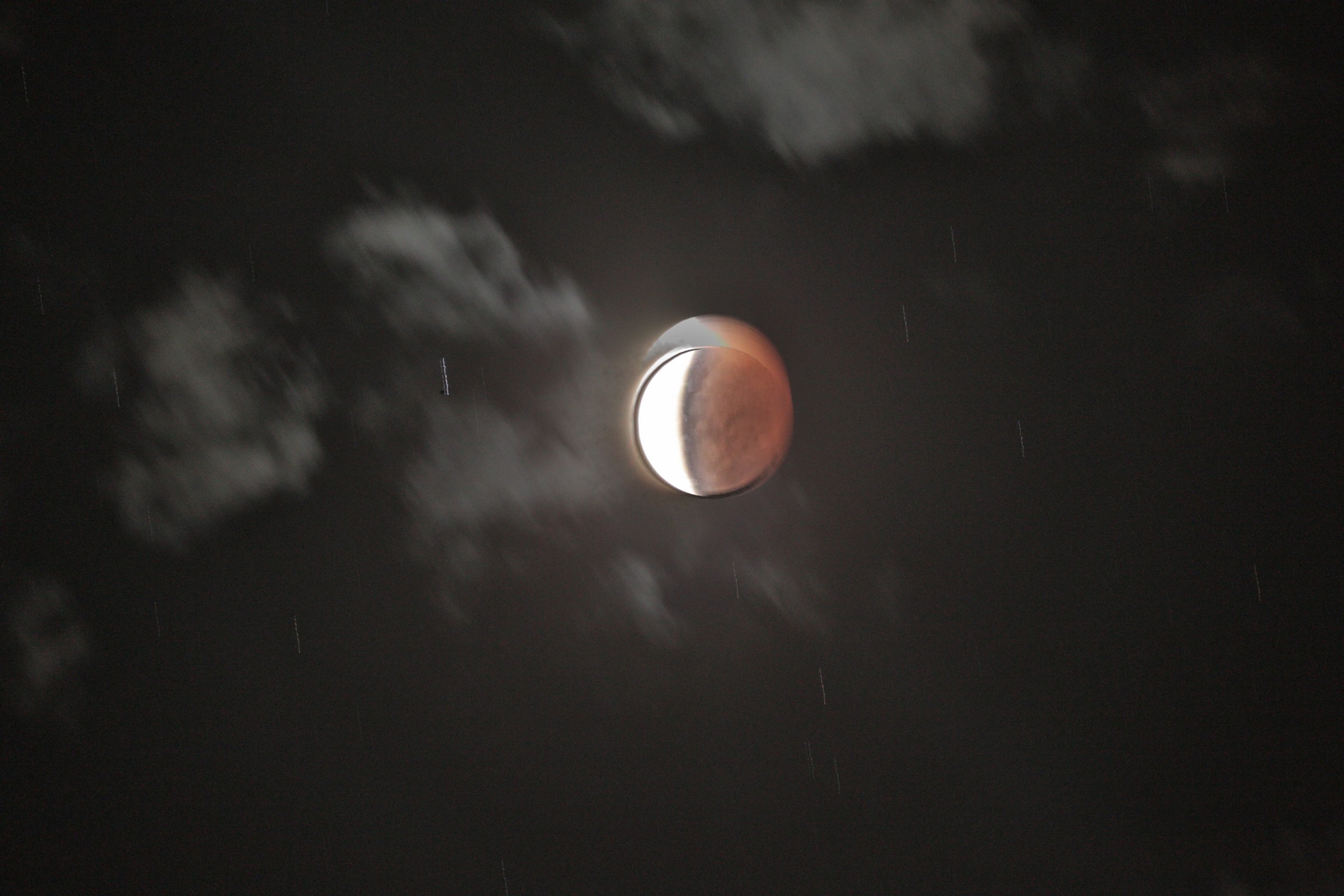 A reddish, partially eclipsed Moon appearing through dark clouds above Brisbane.