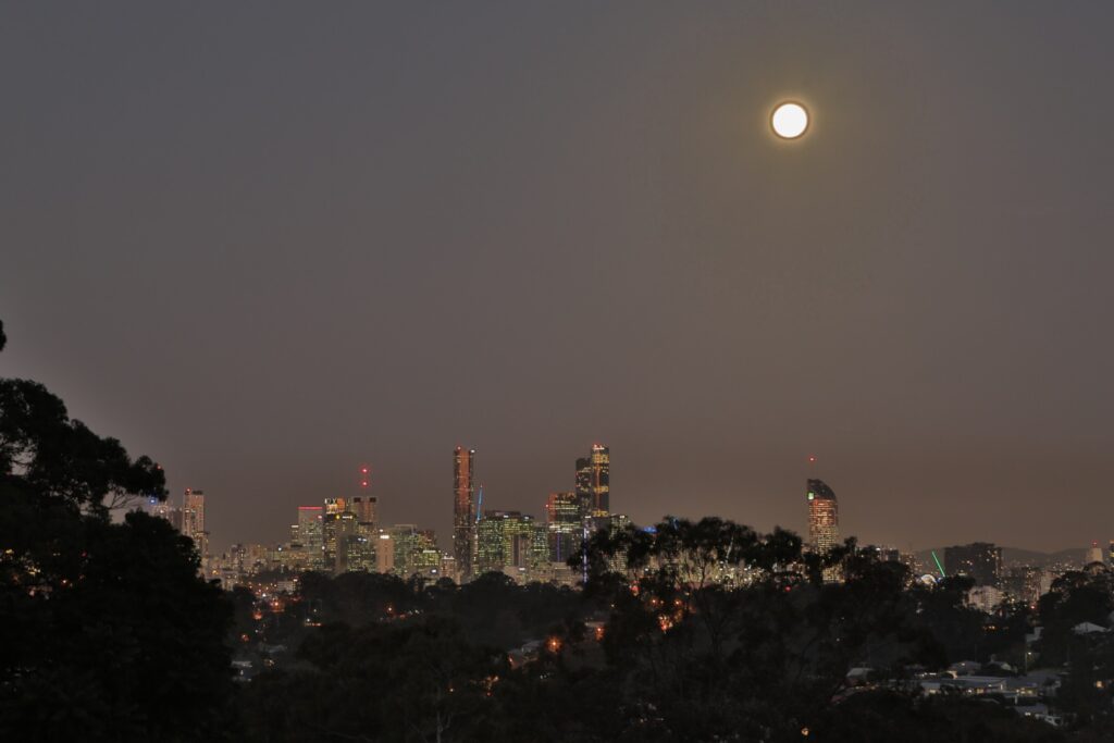 A full Moon rising above the Brisbane skyline in a violet evening sky.